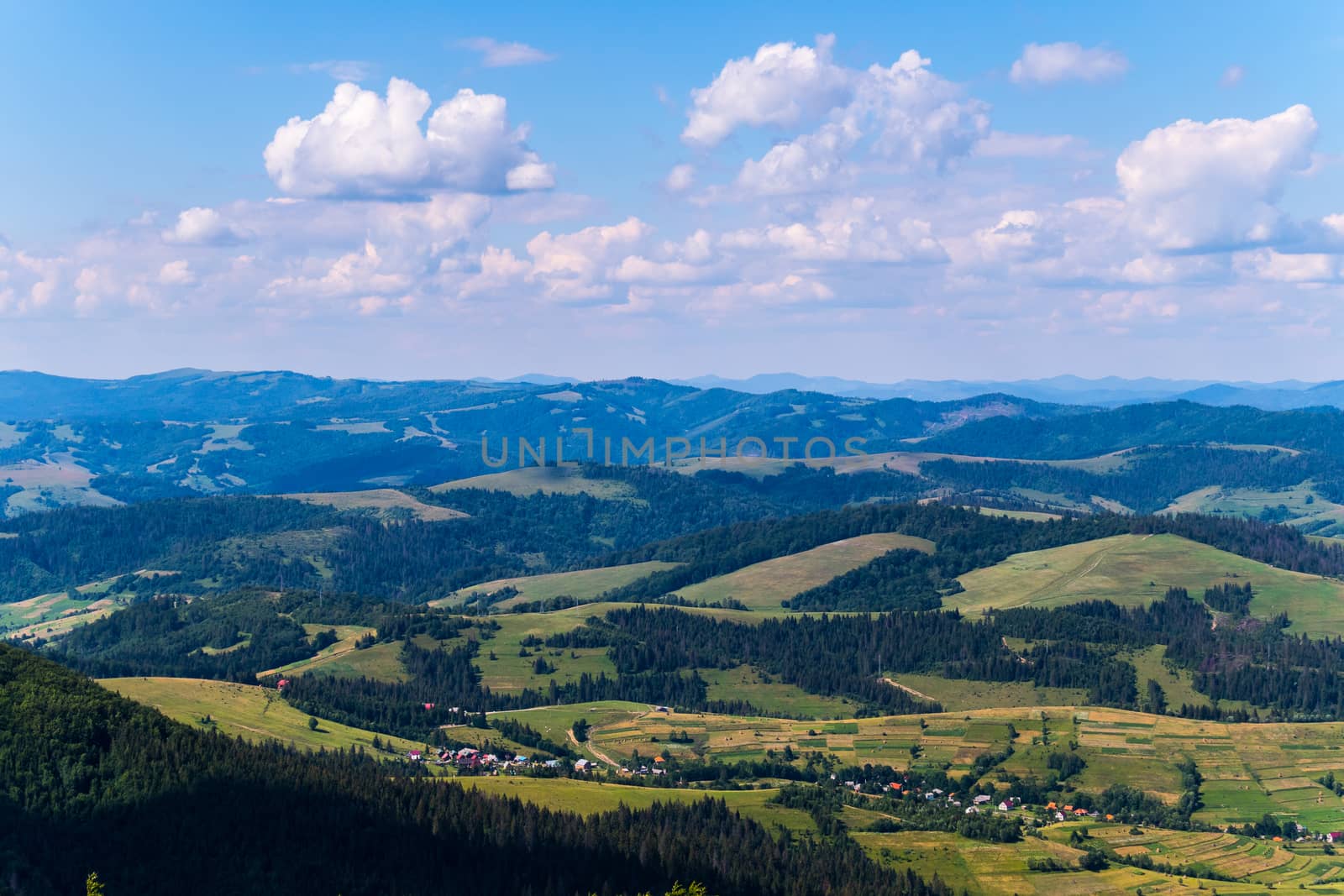 village in a mountain valley, green trees and blue sky with clouds