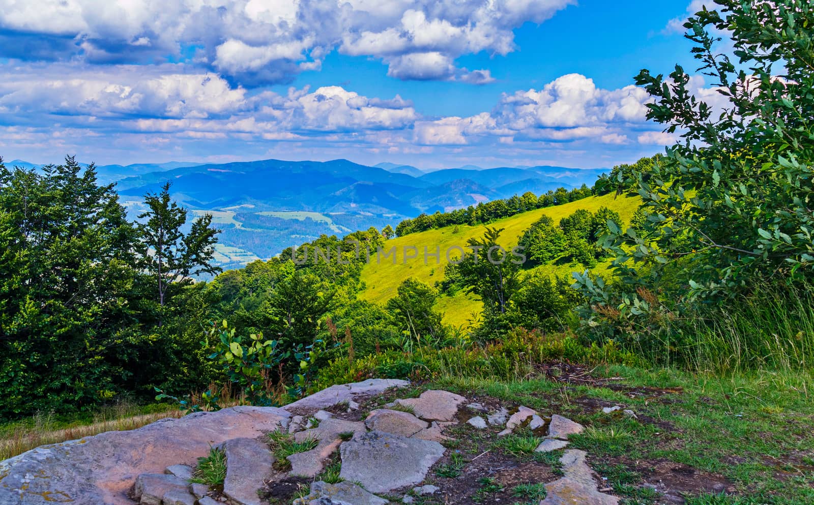 A beautiful view from the glade with stones to the picturesque mountain slopes with the haze of the blue sky in the midday heat.