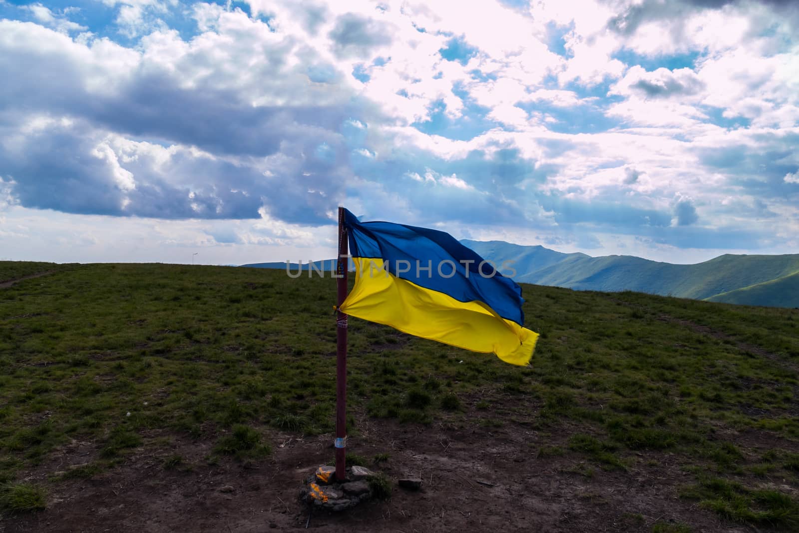 Ukrainian flag, set at the peak of the mountain against the background of a boundless blue sky with white clouds