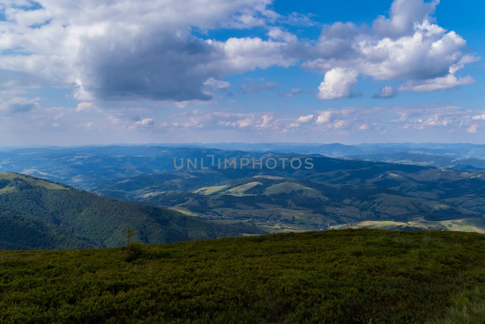A blue, slightly cloudy sky and beautiful, green mountains with a little haze over them by Adamchuk