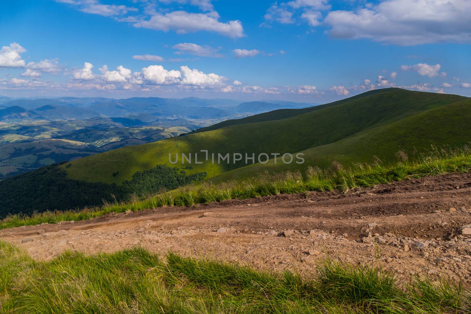 A steep dodgy dusty road leading to the descent from a wide green mountain