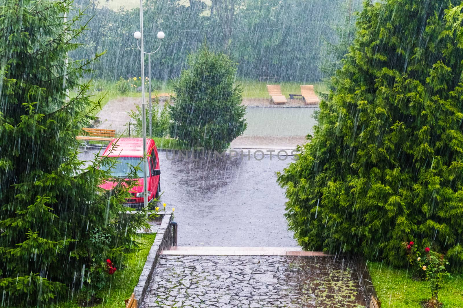 Drops of very heavy rainfall fall on asphalt and trees near the hotel complex