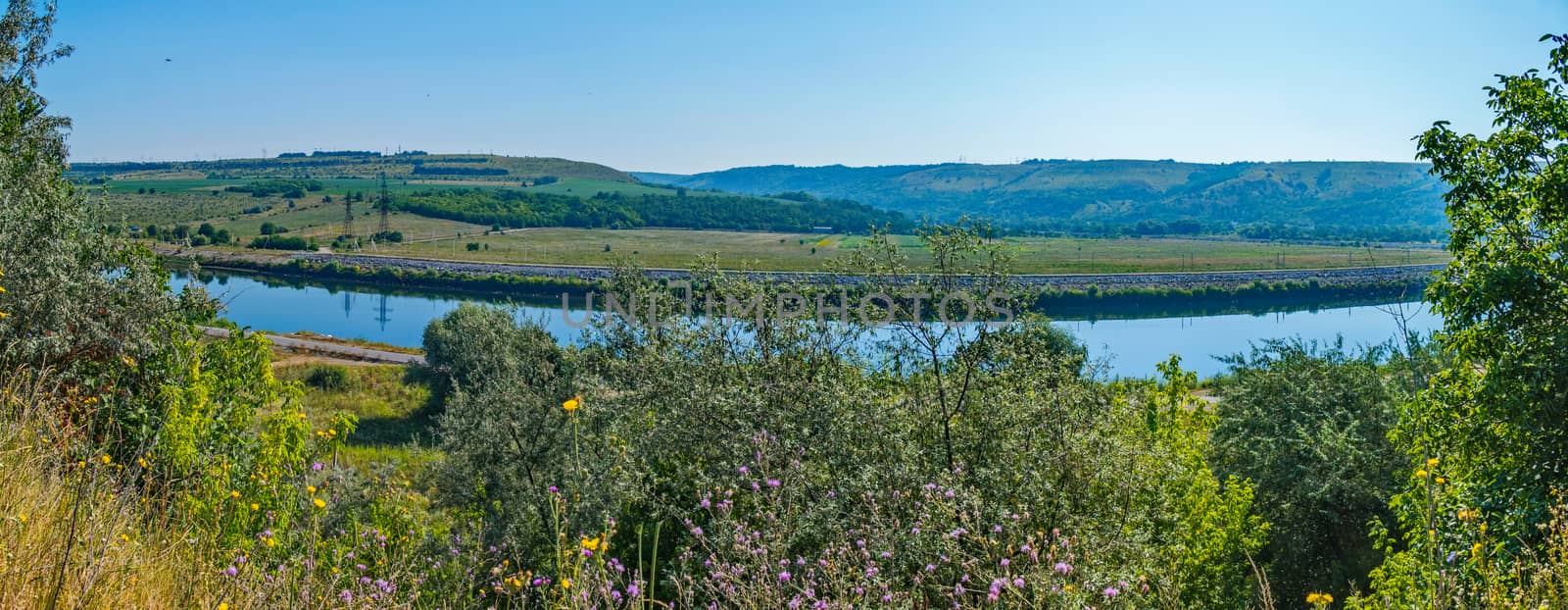 calm blue surface of the river on a sunny day, despite which stretched asphalt road by Adamchuk