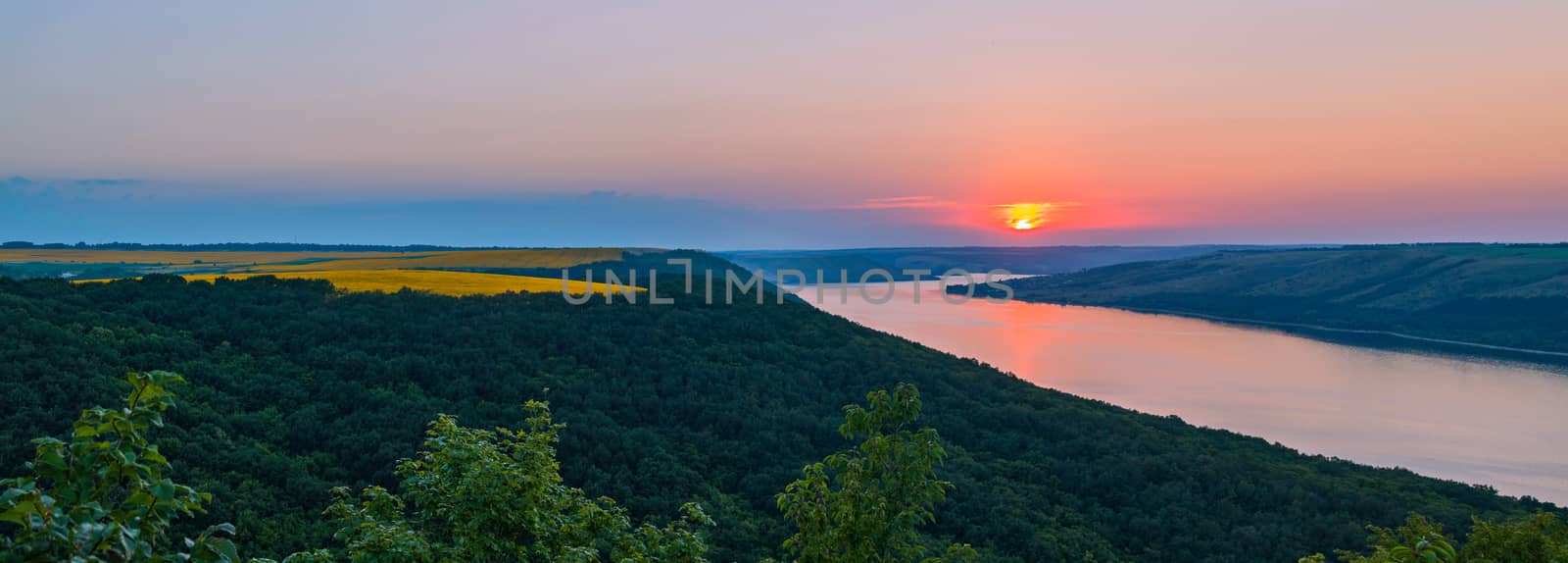 a masterpiece panorama of the setting sun on the river green of the tops of trees and gold of wheat fields