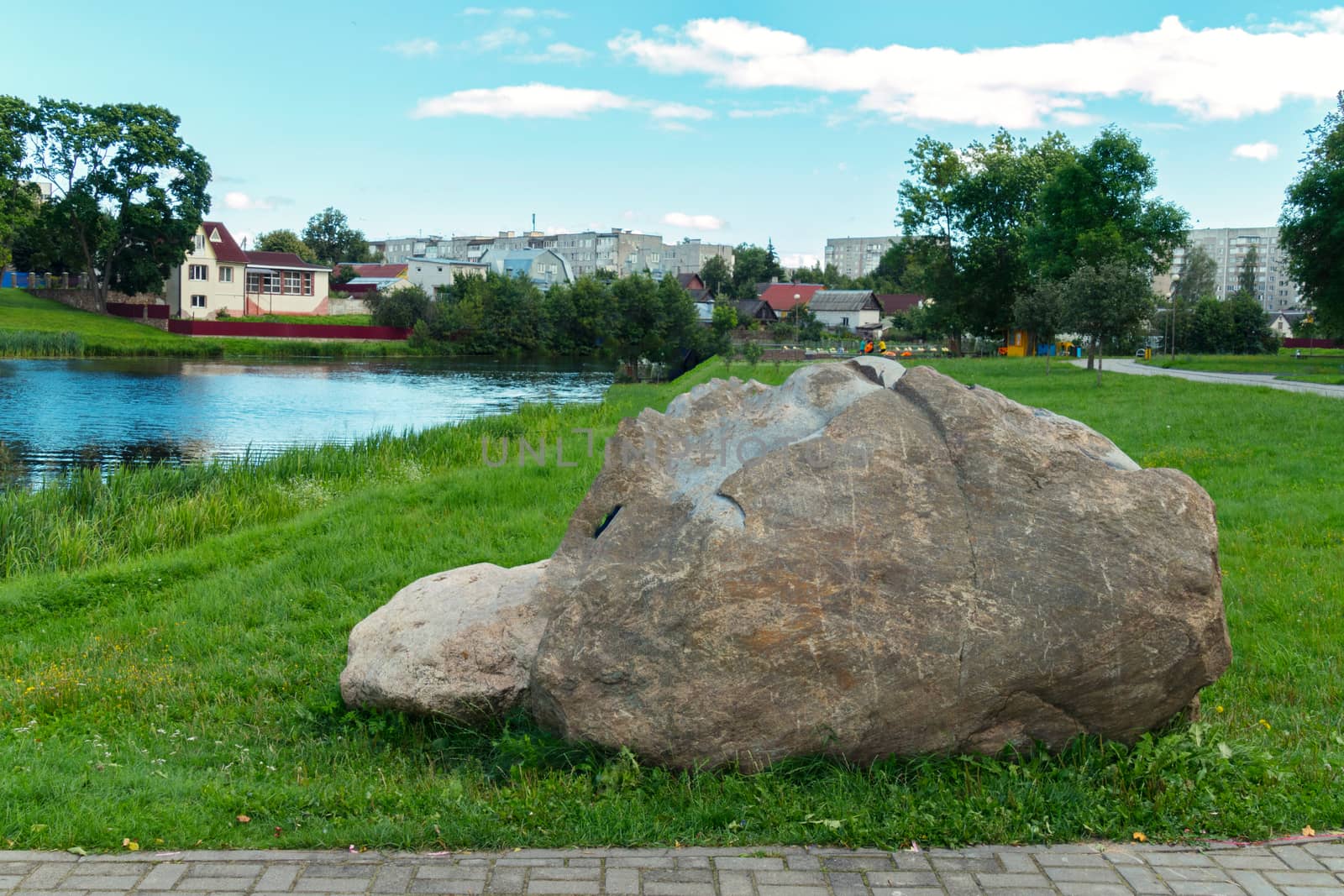 a large gray stone on the green grass near the lake in the city park