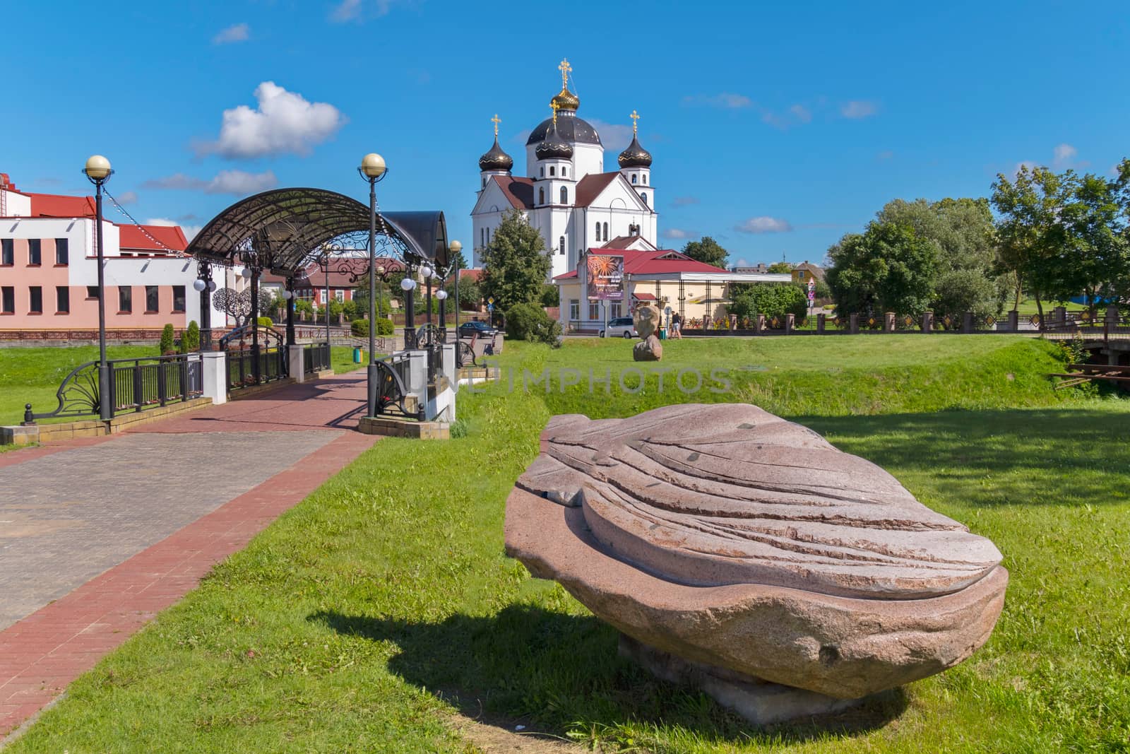 white church on a green meadow with a large stone in the foreground, blue sky, a resting place