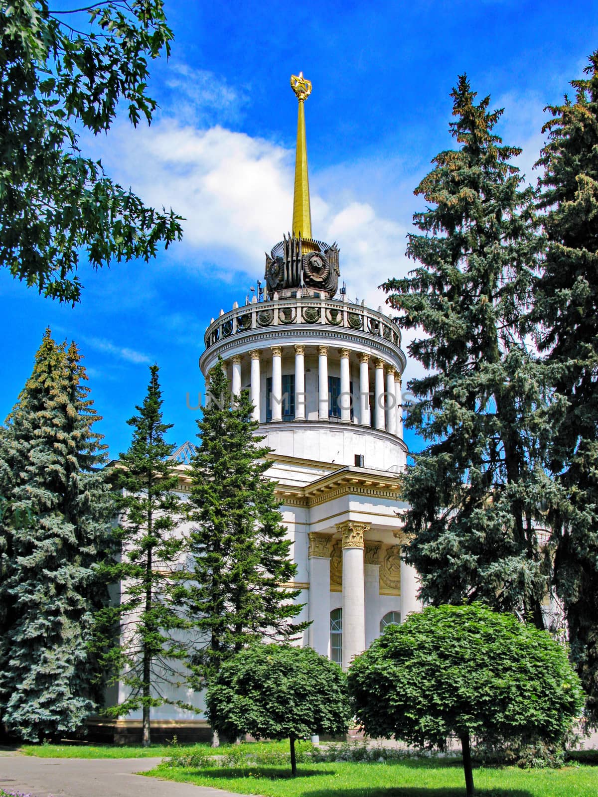 A building with a high tower and columns in the Gothic style. Around the pine and the blue sky