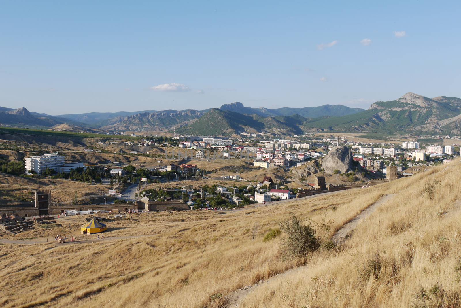a shattered fortress, a circus and houses located in a mountain valley, dry grass. tourism