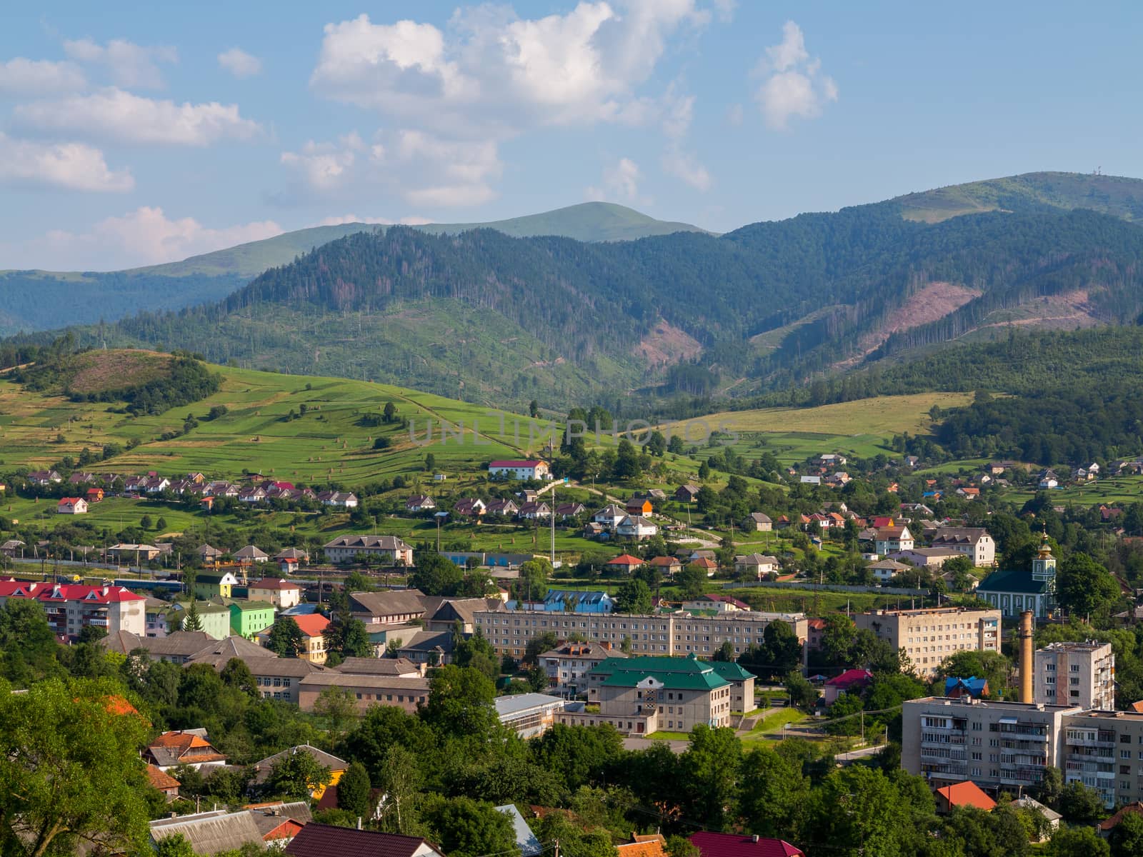 Nice view of the houses and roofs of the streets of a small town lying in a green mountain valley under a warm summer sun.
