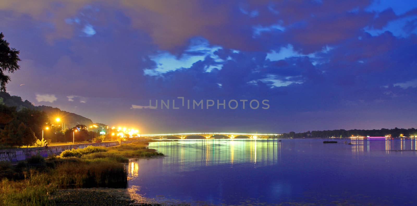 Brightly glowing car bridge against the background of the evening sky, connecting the two banks