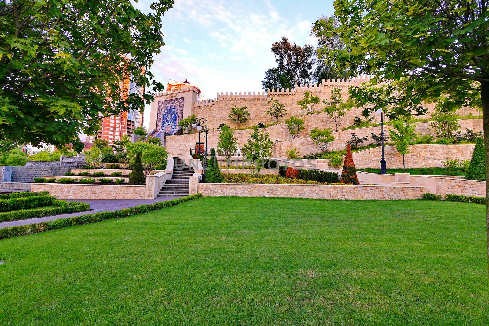 A beautiful park with an emerald green lawn next to flower beds with flowers located on the sides of the stairs with steps going up.