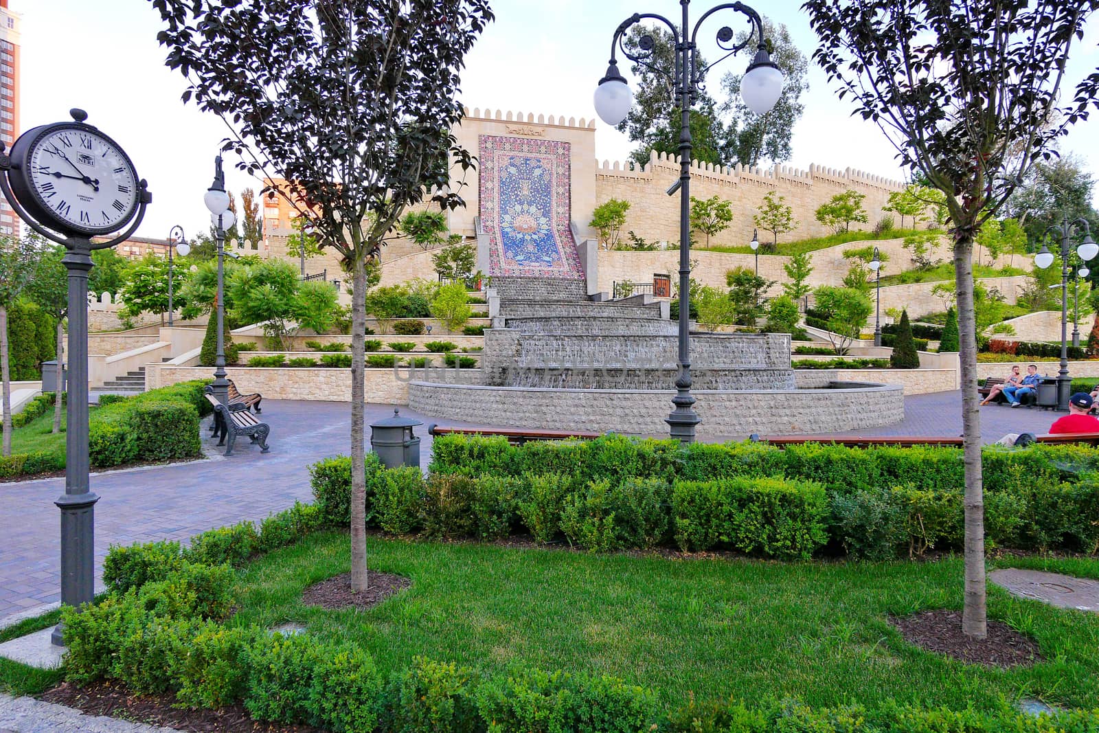 people resting in the park on a bench in front of a stone wall with a lined pattern and a clock on a lamp post