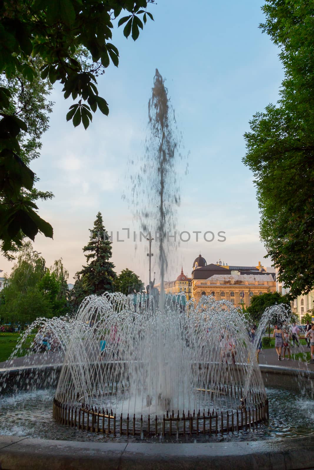 The high spray of a fountain flying over the background of a blue sky in the city park spill over