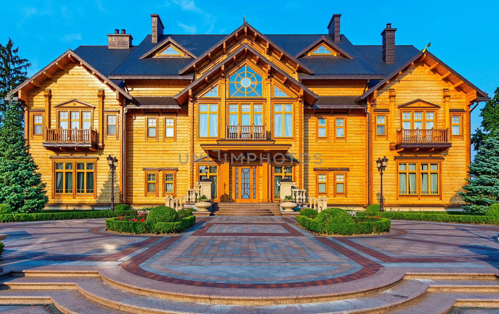 The area is laid out with beautiful patterns from the tile with a green lawn growing on it in front of the house with sheathed wood and windows of different shapes.