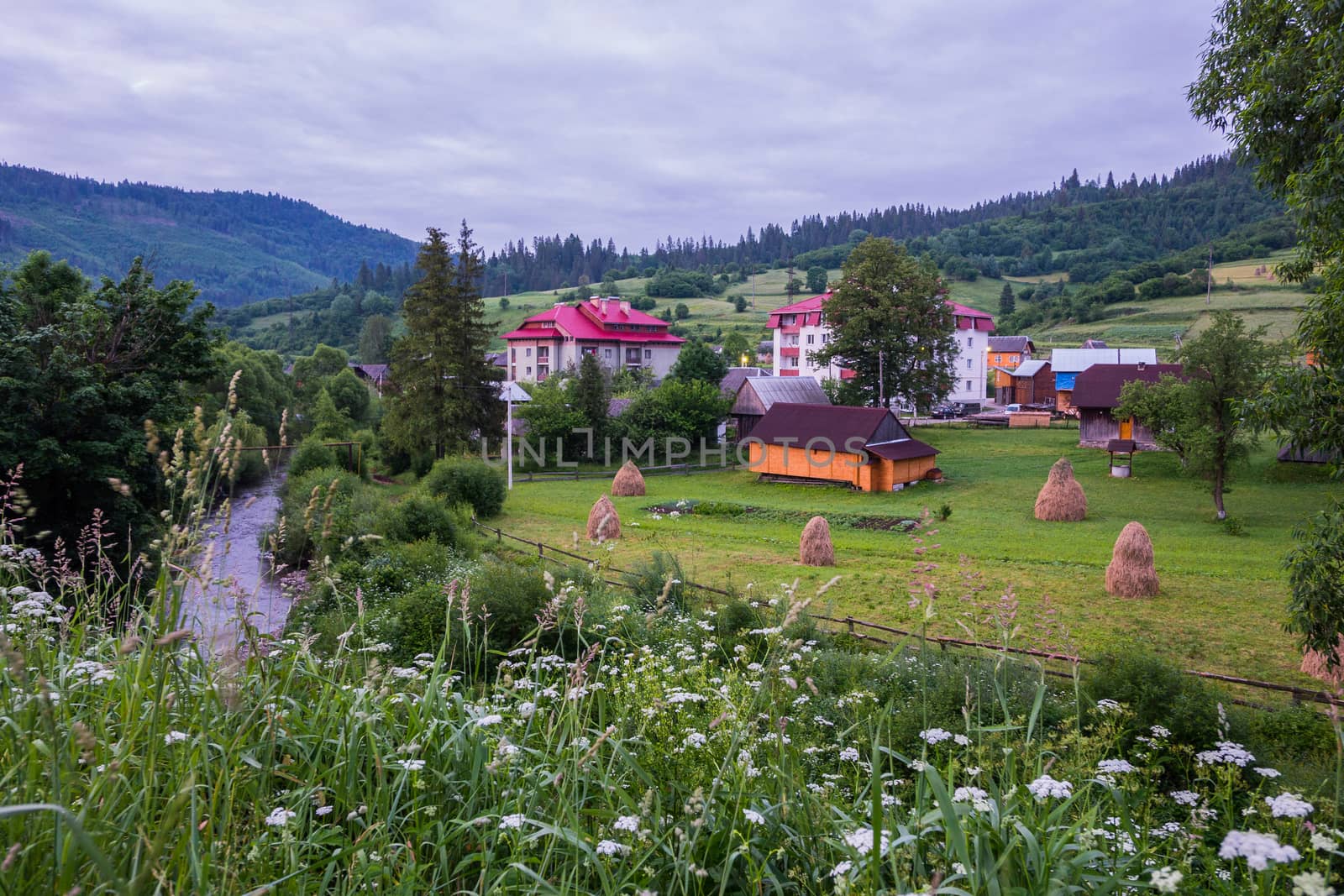 cottages for recreation on a green meadow with haystacks in a mountain valley against the backdrop of green mountain peaks and a cloudy sky. a place for recreation and tourism