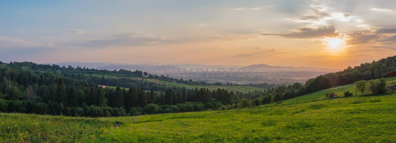sunset over a panorama of mountain hills and village in the valley by Adamchuk