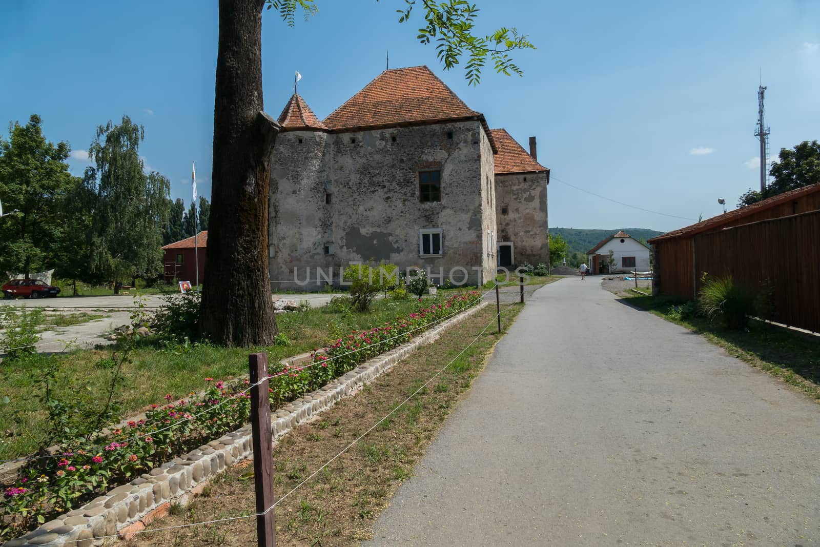 An old, gray building with a tiled red roof and a road around it