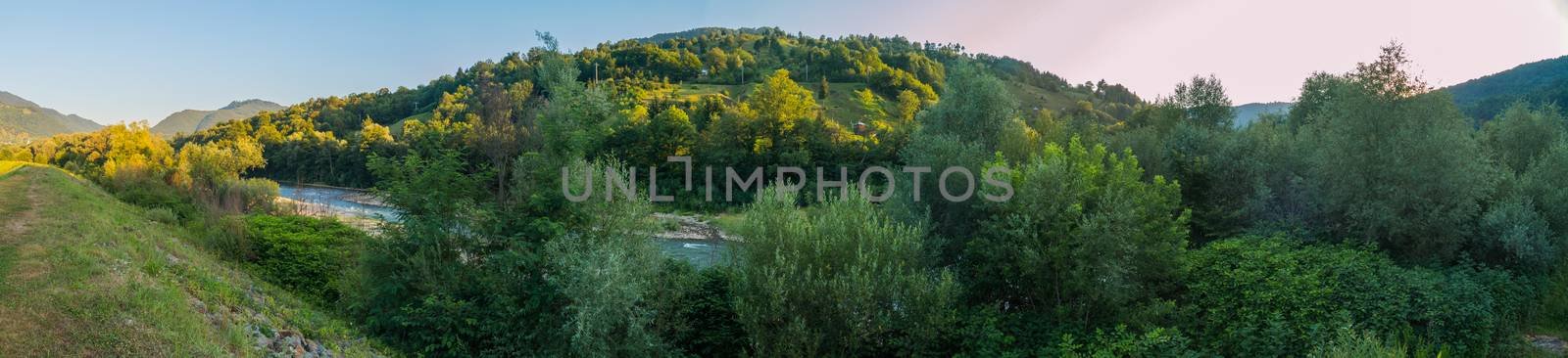 A small fast river against the background of large green hills and mountains with trees