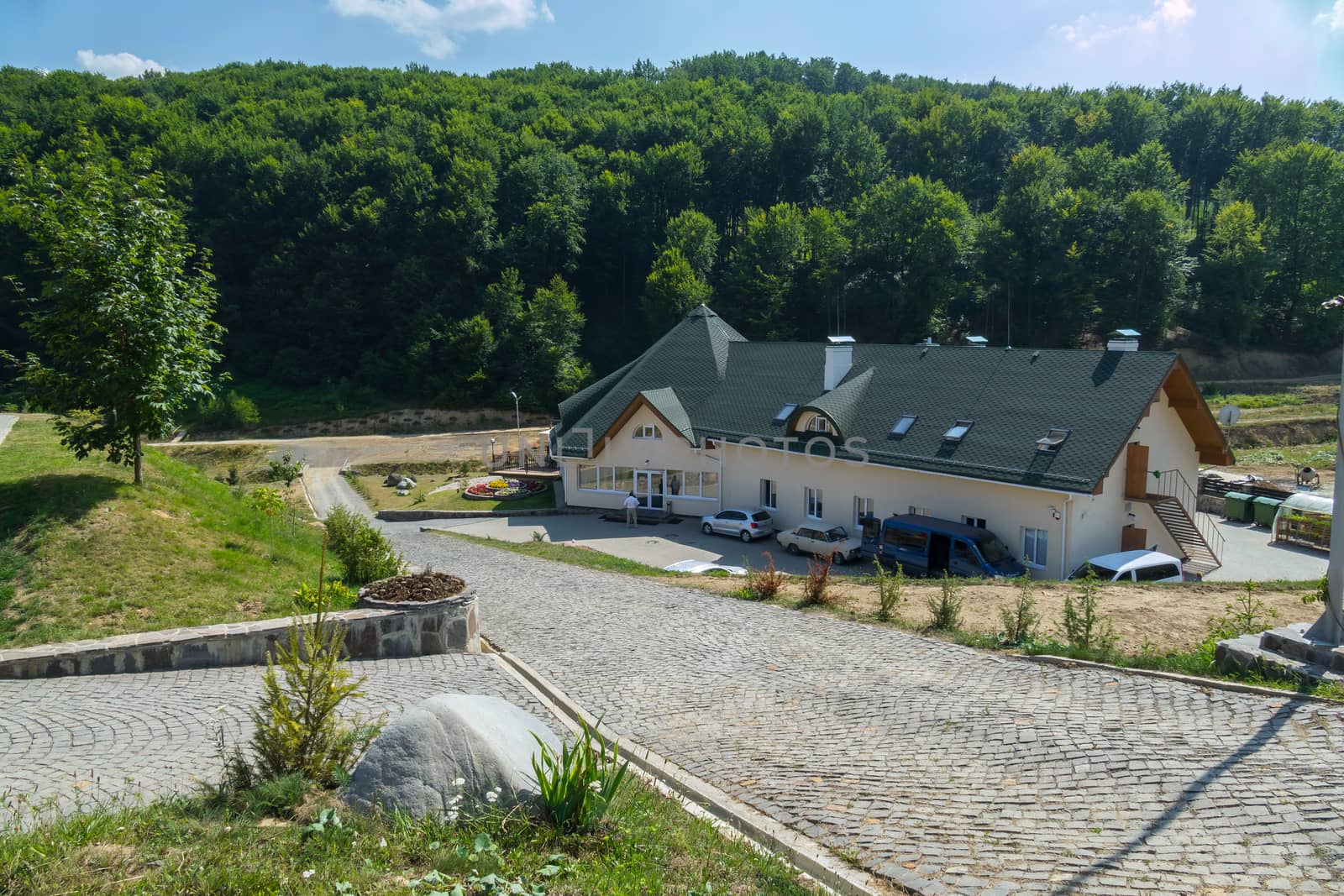 The access road from the cobblestones leads to a large house, a hotel drowning in green trees against the blue sky