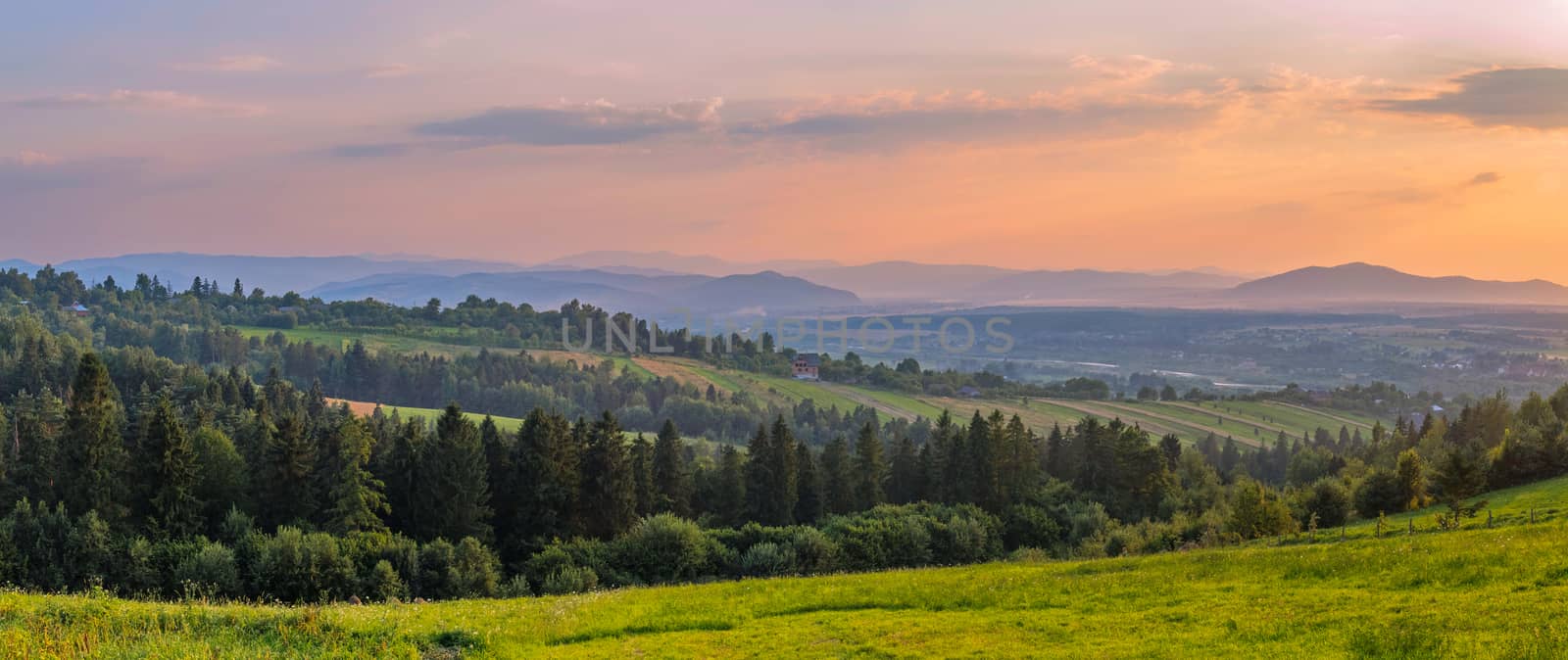 Elegant panorama of the mountainous terrain with valleys forest planting beautiful peaks in the distance against the background of the evening sky. by Adamchuk