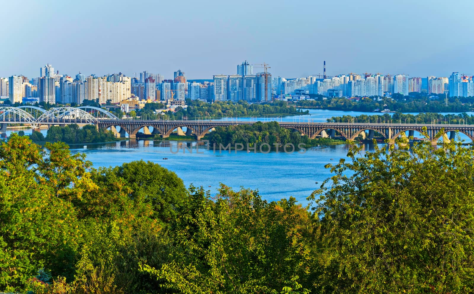 A magnificent landscape with a bridge going through a wide river against the backdrop of city skyscrapers.