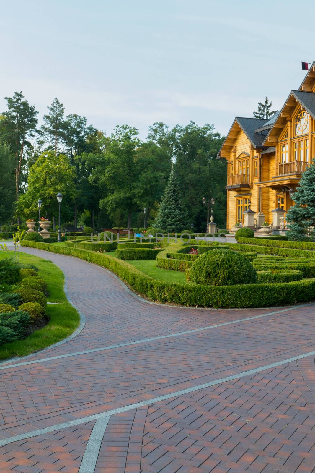 The alley is laid out with a red cobblestone in a well-kept park near a beautiful wooden house