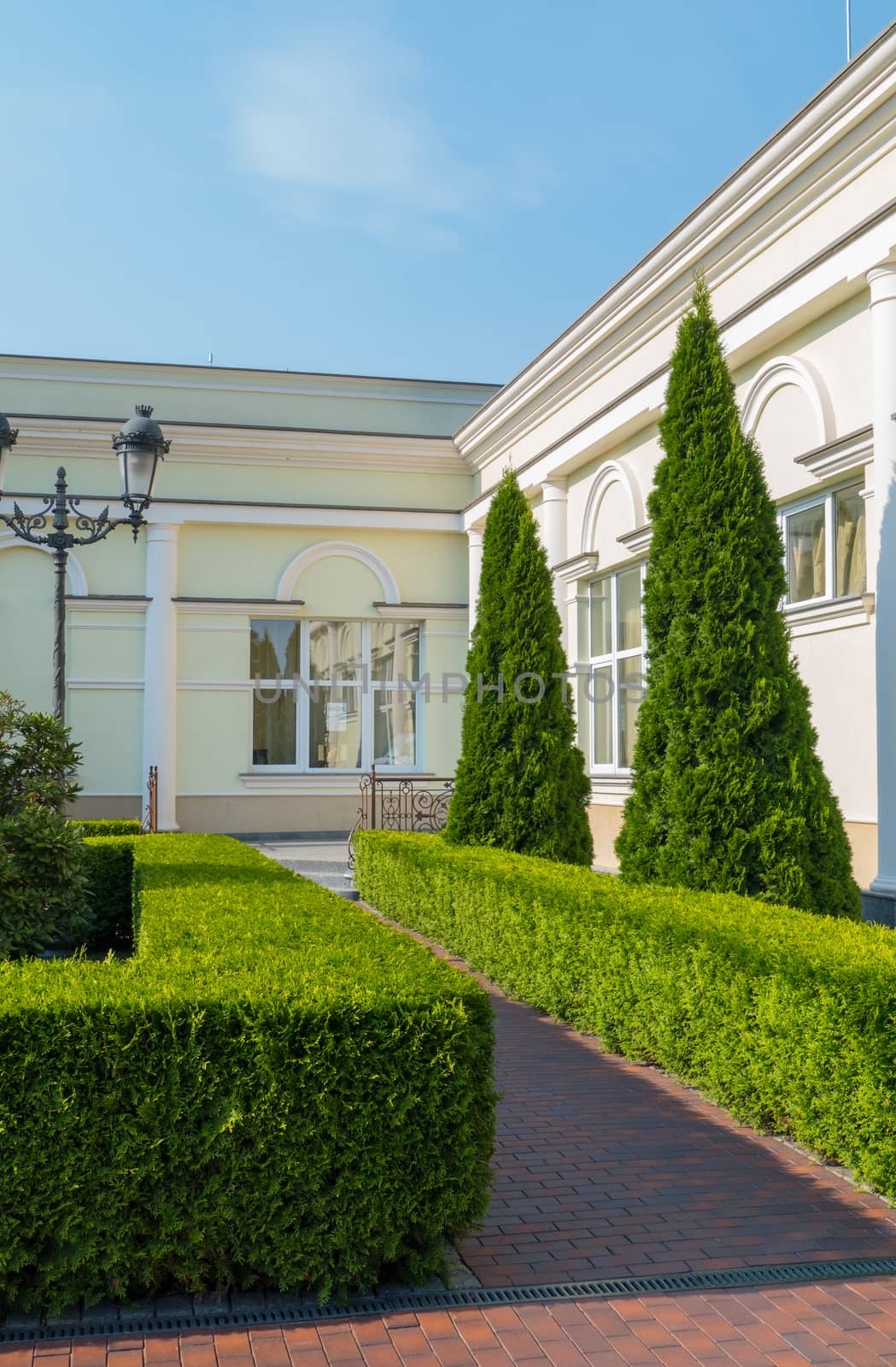 white private residence with a beautiful well-groomed territory, on which grow pyramidal thai, neat trimmed shrubs, lantern. against the blue cloudless sky