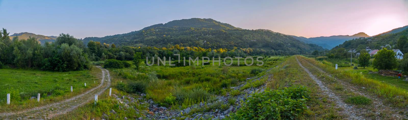 Panoramic view of the green valley with trails on the background of the mountain and the setting sun