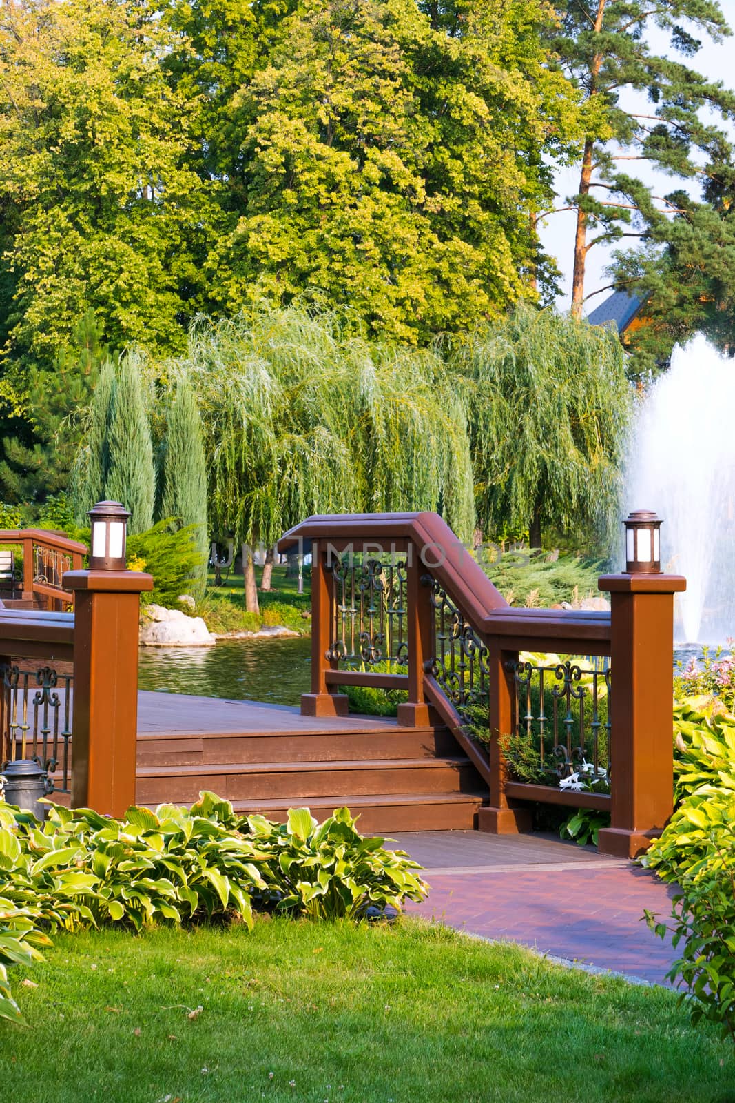 Stairs to a wooden bridge with railing through the river in the city park near the fountain of the wreath of willow