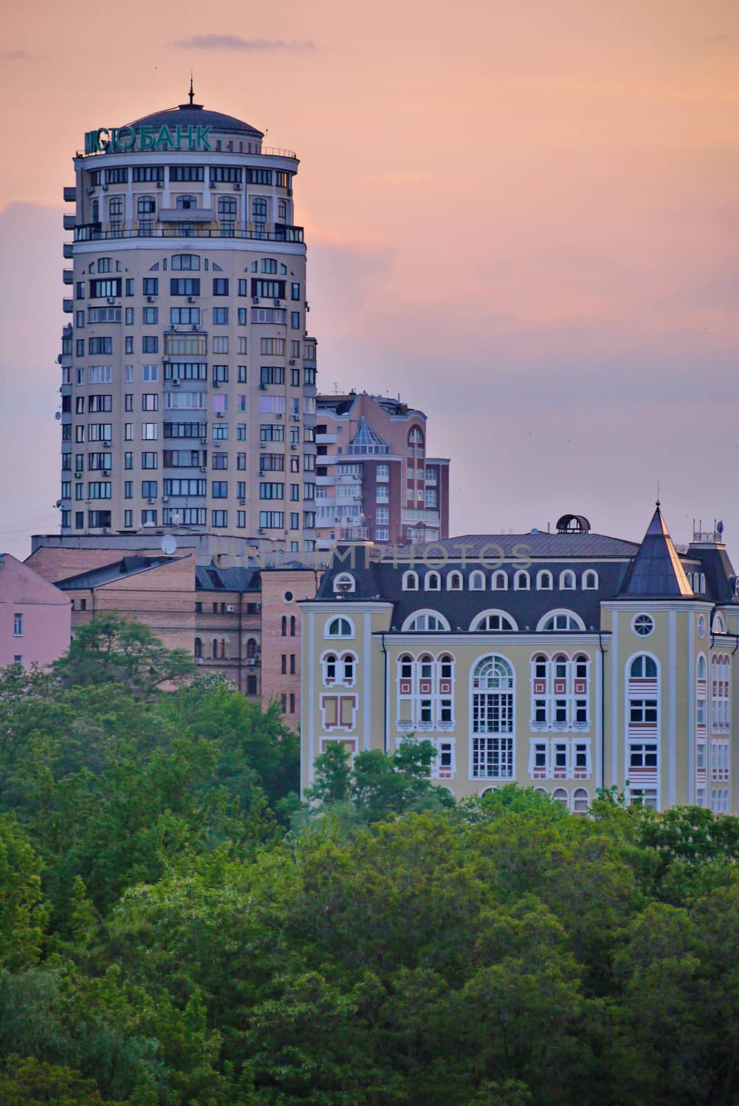 High urban high-rise buildings against the background of green trees and the evening sky