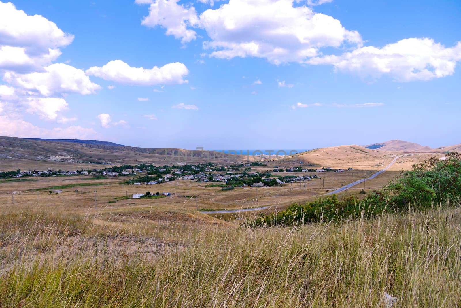 a landscape of vague gray hills and a settlement in a valley with a narrow strip of sea blue in the distance
