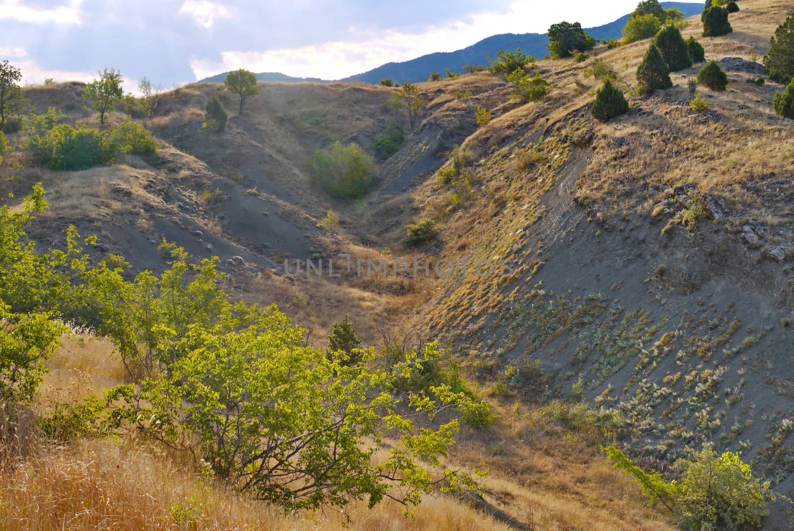 A steep sandy descent from a hill on a background of huge green mountains.