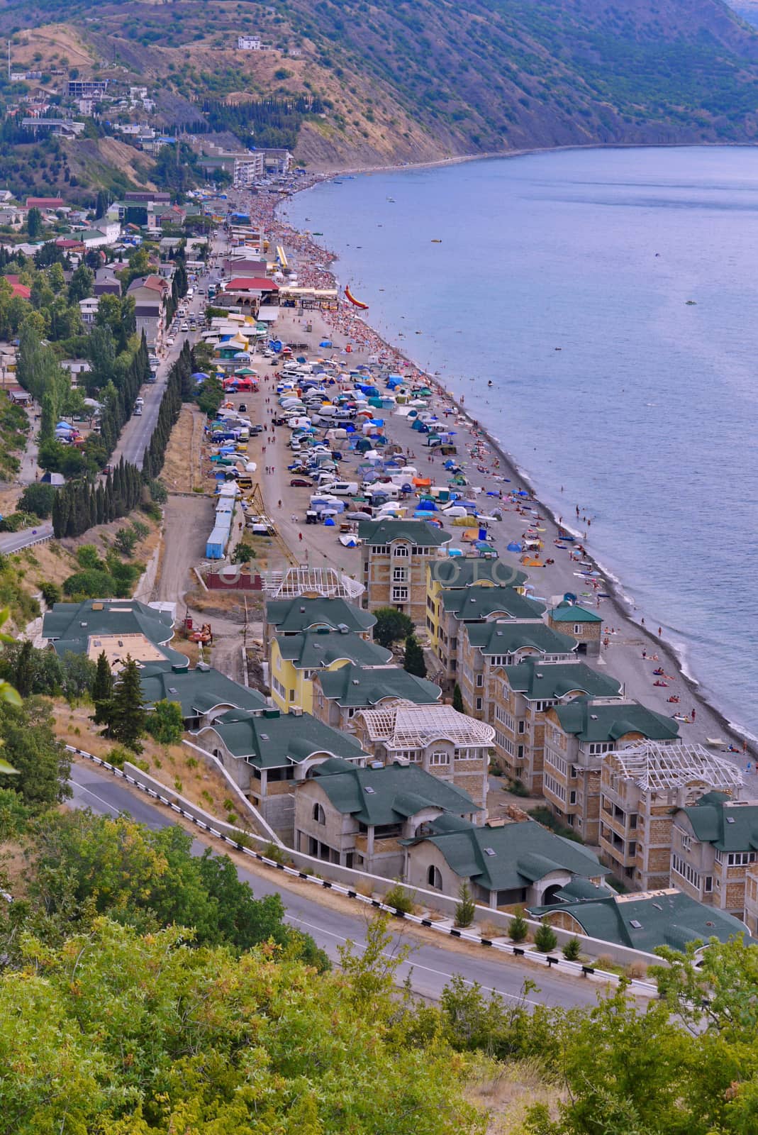 a sea bay with a beach on the sandy beach and a large number of hotels and cars