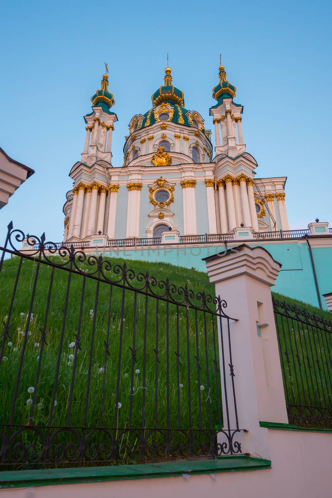 A tall temple with golden domes surrounded by a fence made of wrought iron