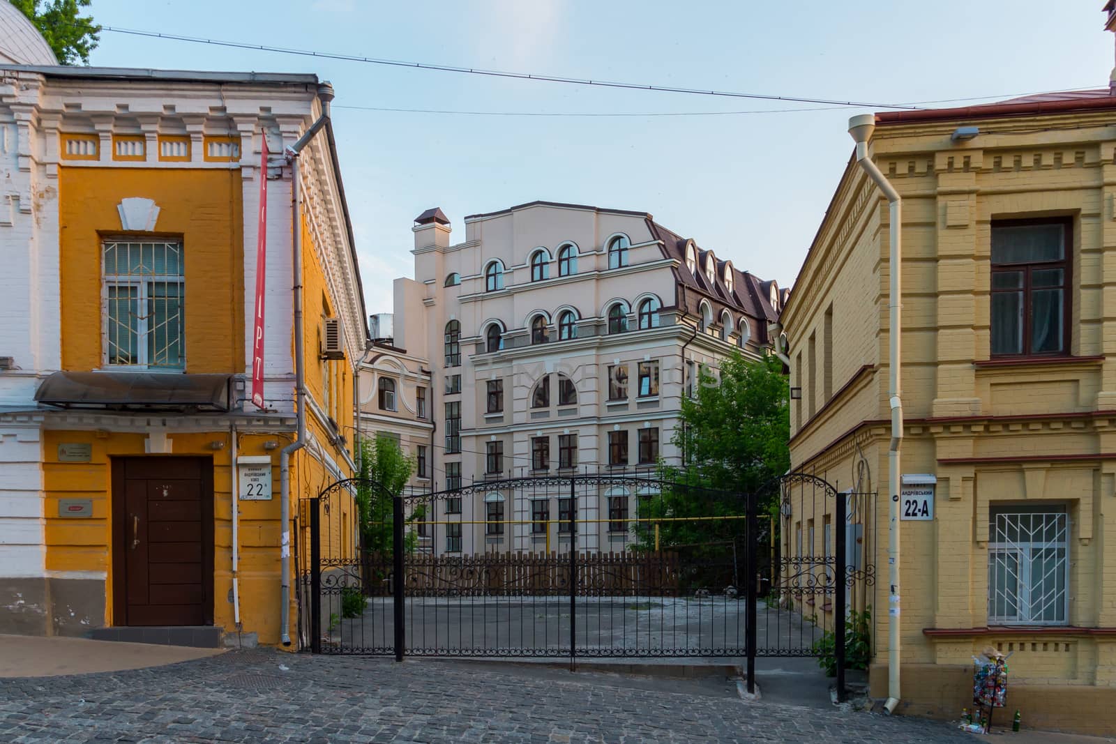 Forged gates between two buildings of cream color against the blue sky
