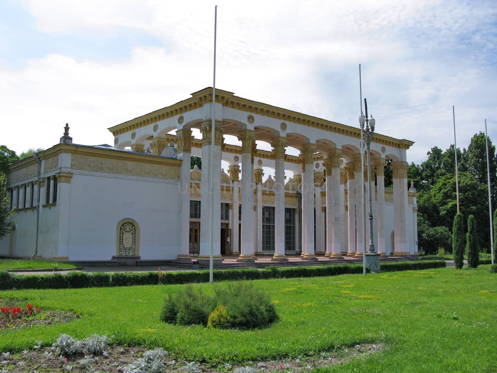 building with white columns and walls with a pattern on a green lawn in the park by Adamchuk