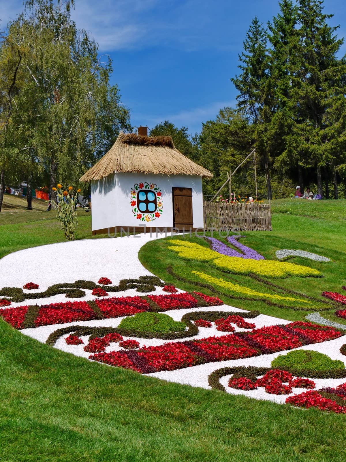 beautiful lawns in a park with flower beds in the form of a national ornament and a decorative house with thatched roof