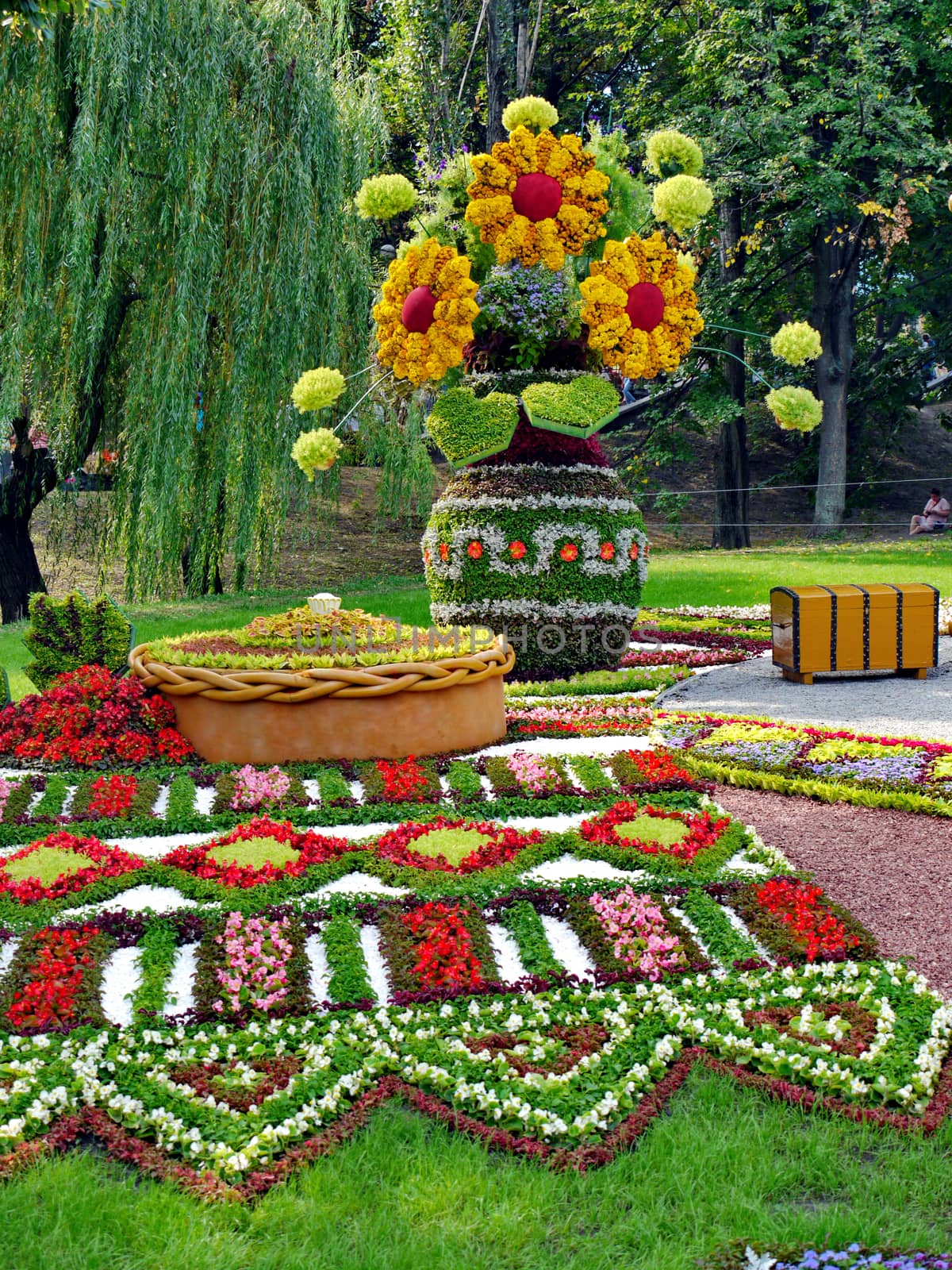 figures from bright multicolored flowers on a flower show harm green trees. a towel, a loaf, a bouquet in a vase and a chest