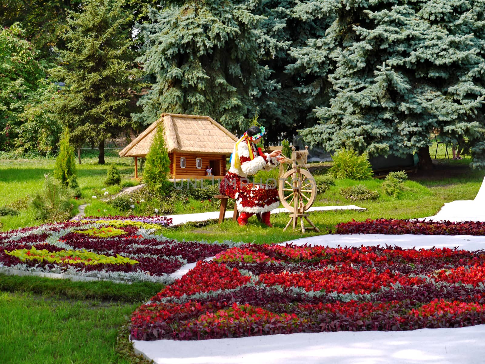 Girl-weaver in national Ukrainian clothes near flowerbeds with flowers on the background of the Ukrainian village house.