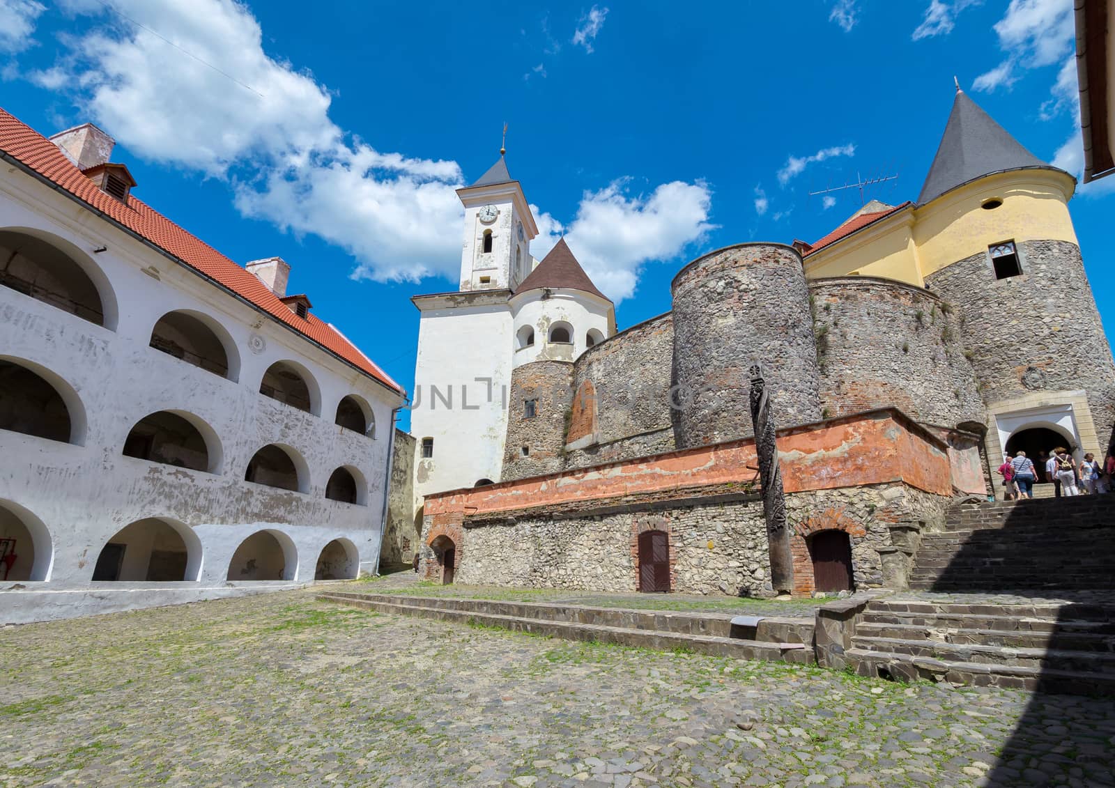 The courtyard of the ancient fortress is paved with stone. With tourists going to the exit on the steps of the stairs.