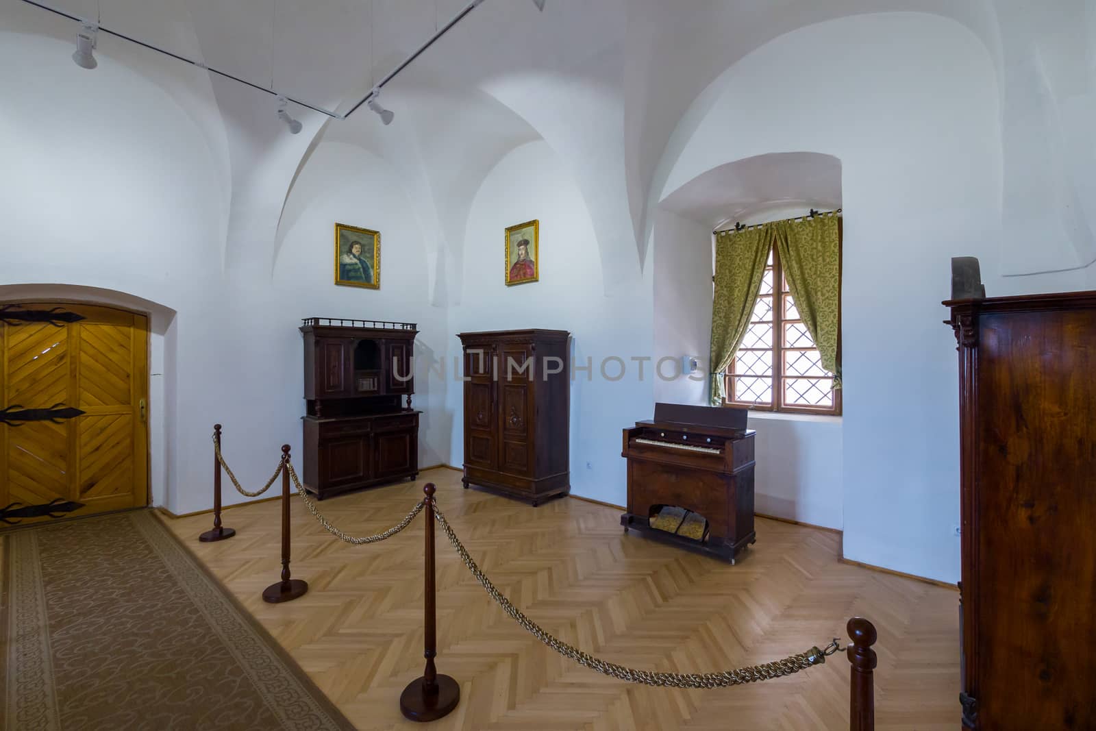 white museum exhibition hall with rarity wooden furniture, portraits and a window with a green curtain