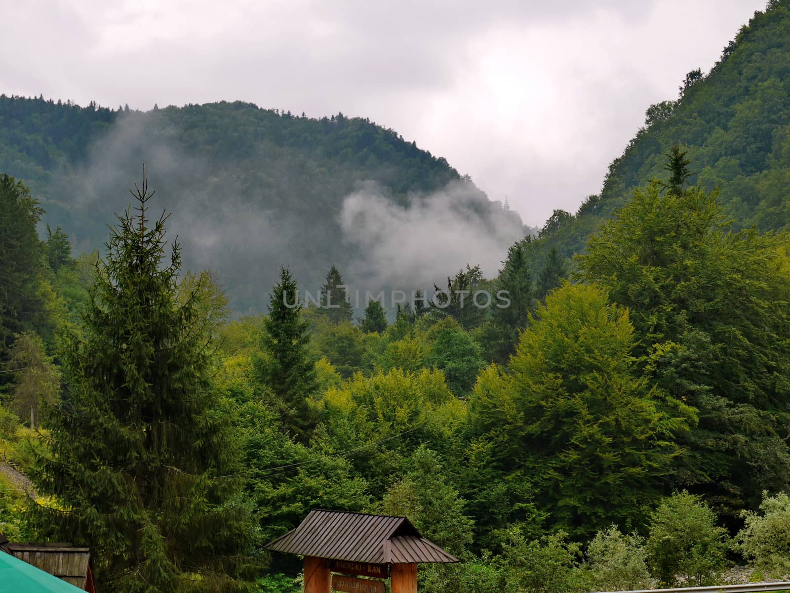 Mountain peaks in the haze of mist and the roof of the well at their foothills by Adamchuk