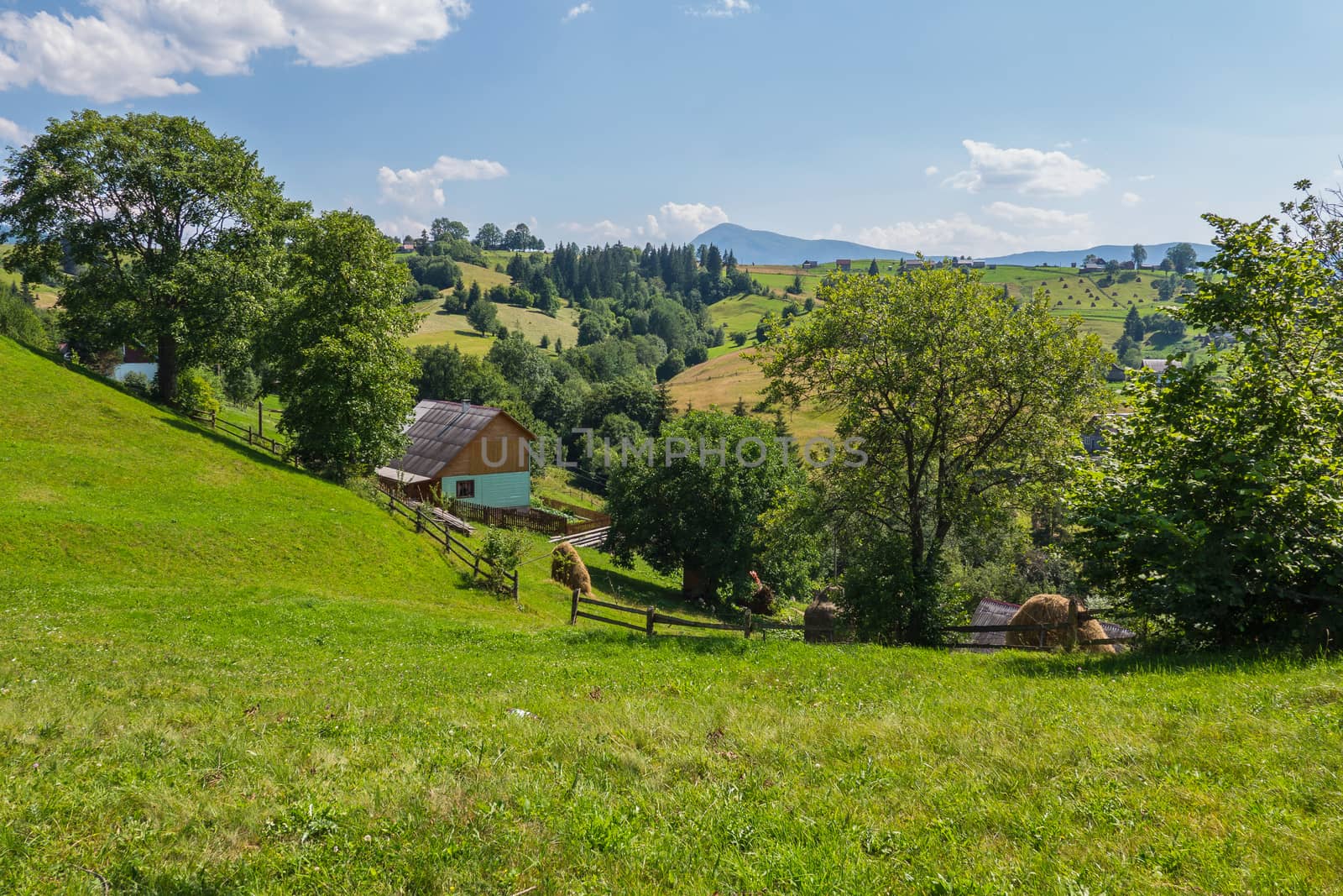 A scenic landscape of bright green grass near the house between the hills under the blue sky