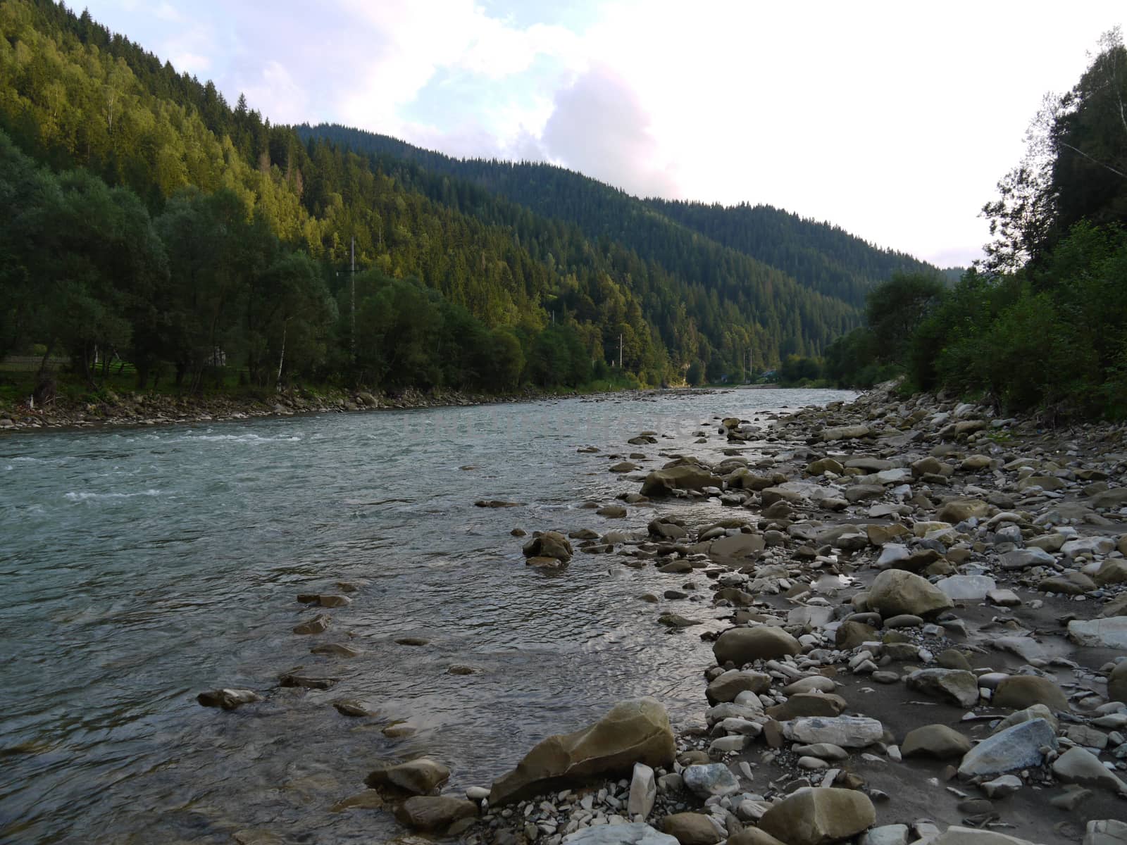 a shallow mountain river with clear water strewn with stones running between picturesque green slopes