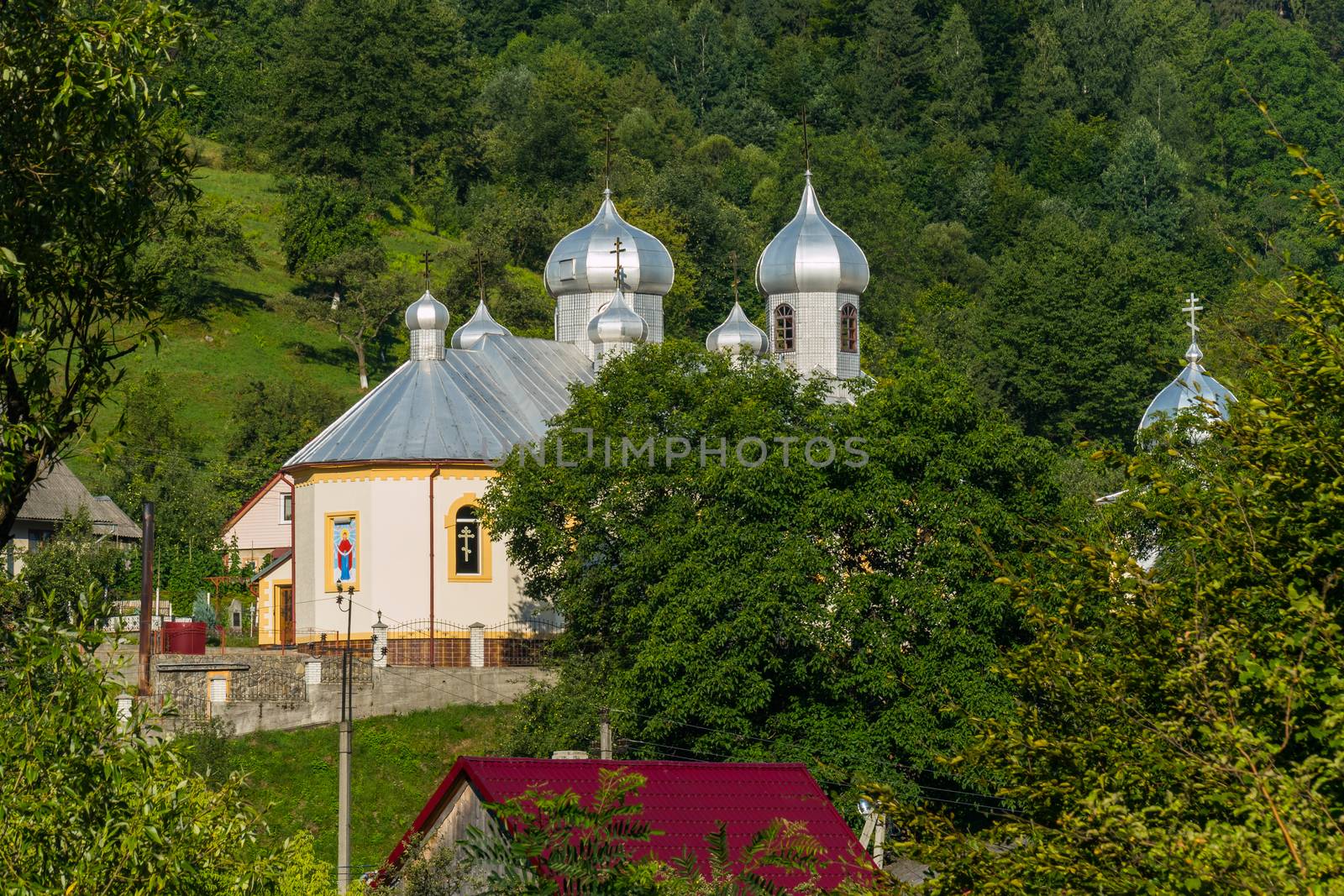 A neat church with white walls and shining domes in the sun. Located in a picturesque countryside amidst beautiful nature.