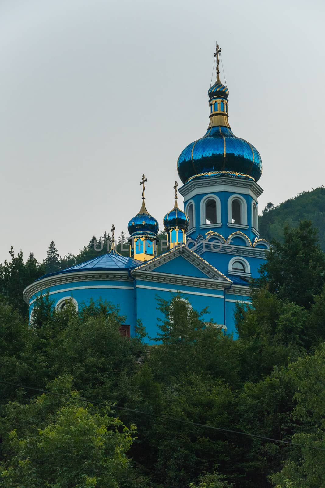 blue orthodox church among green tall trees under a blue cloudless sky