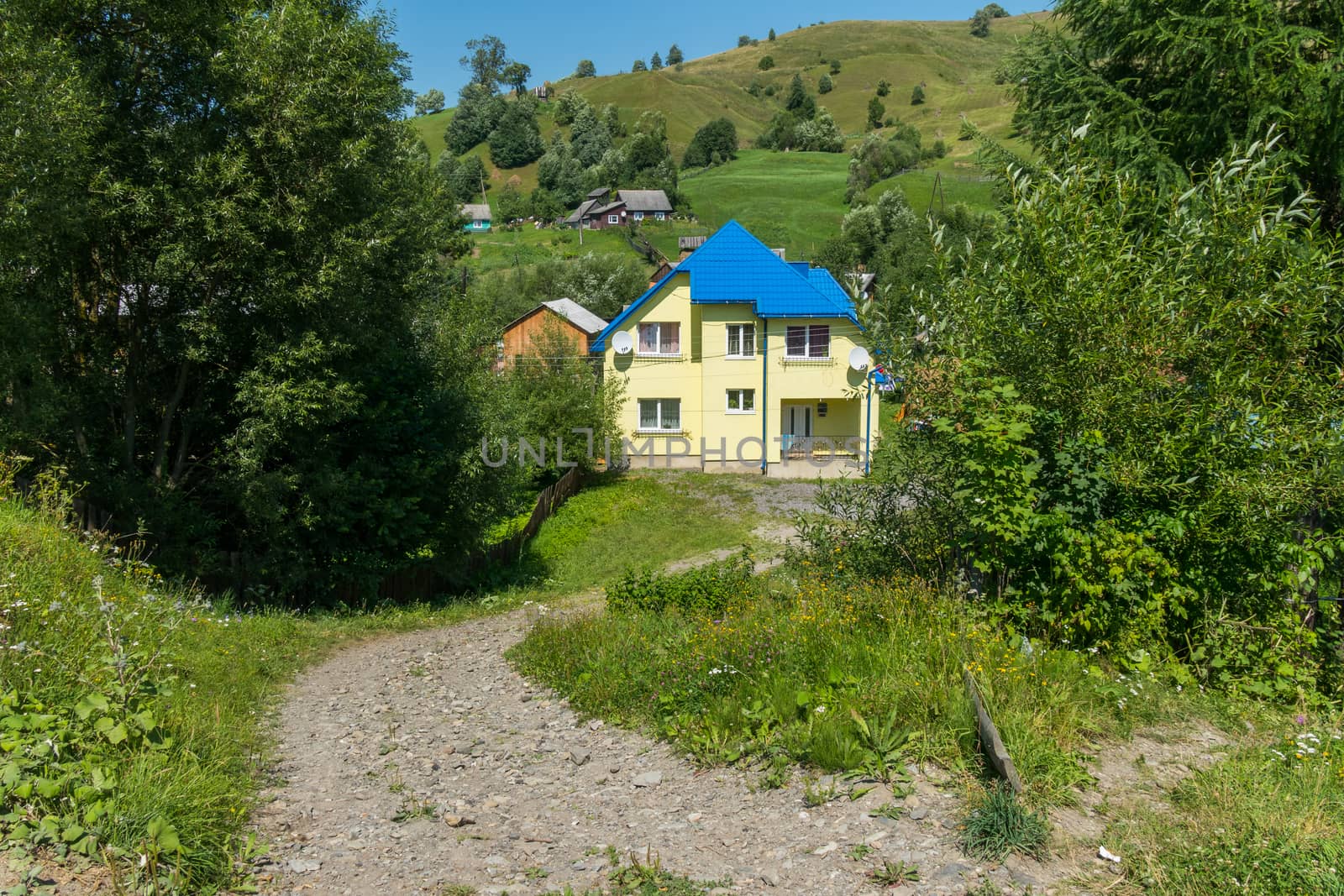 The road in the countryside is strewn with gravel leading down to the house in two floors with a tiled roof and two satellite dishes.