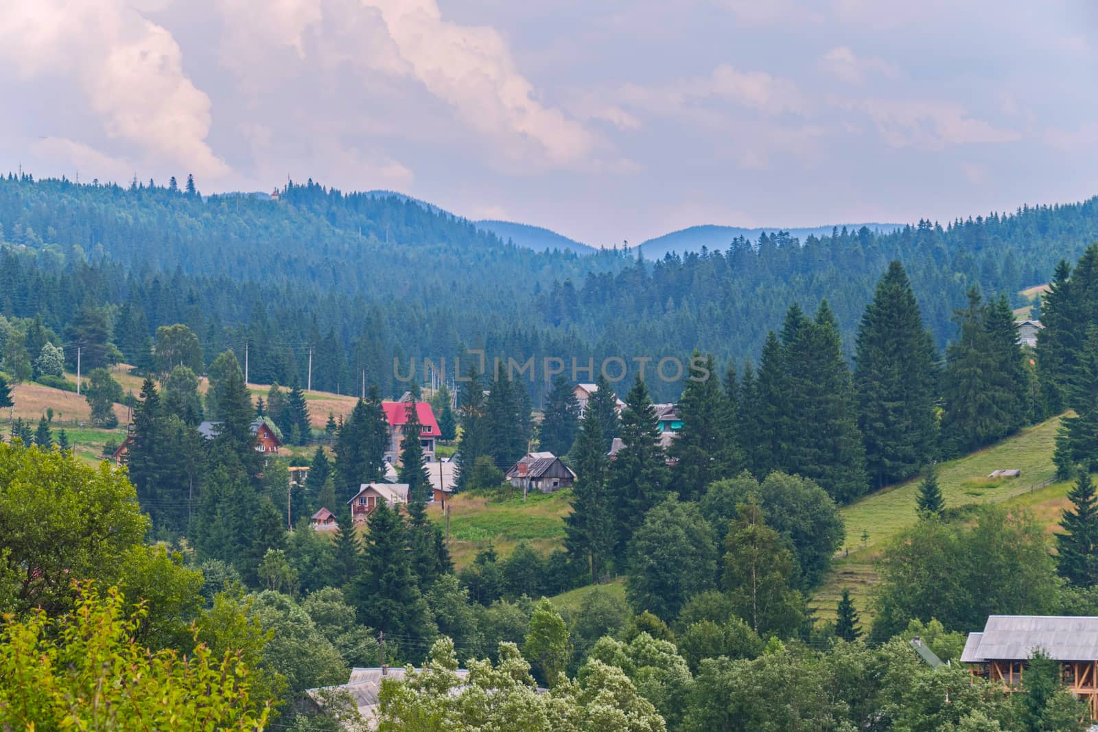 greens of forests and mountains of blue sky with clouds and a small village in the valley