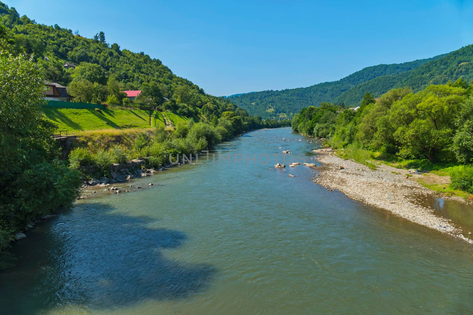 Houses of rural roofs are seen between the trees located in a picturesque place on the slope with the current below the river.