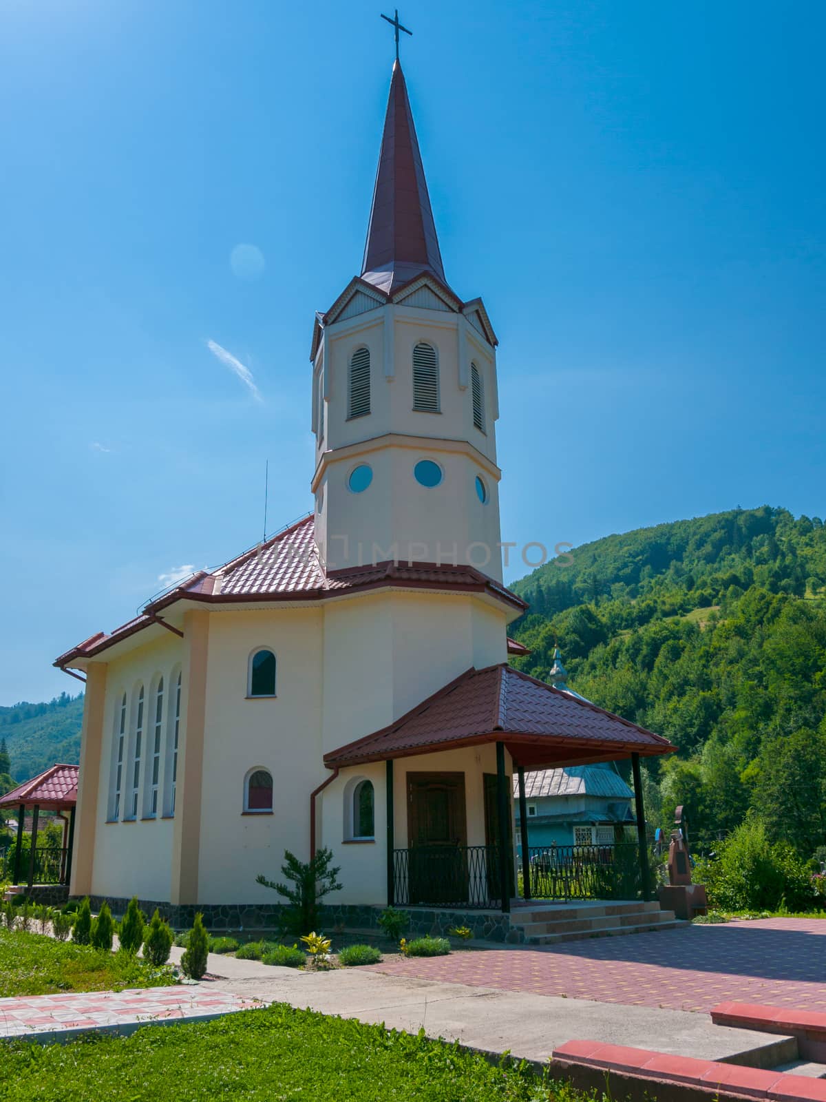 Beautiful modern church with a red roof and a big tower on a background of a green mountain